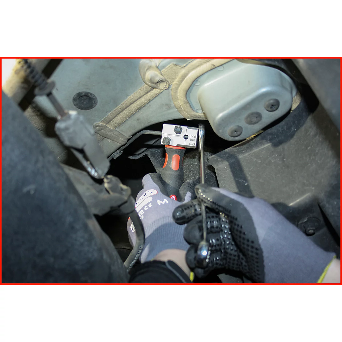 Hände mit Handschuhen verwenden Werkzeug, um etwas unter einem metallischen Fahrzeugteil zu bearbeiten.